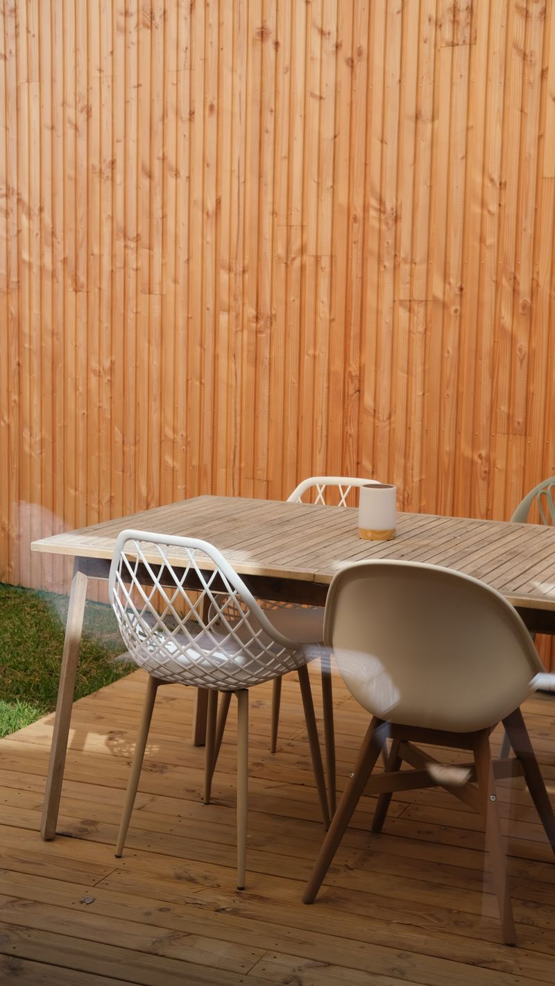 A wooden patio table with white outdoor chairs